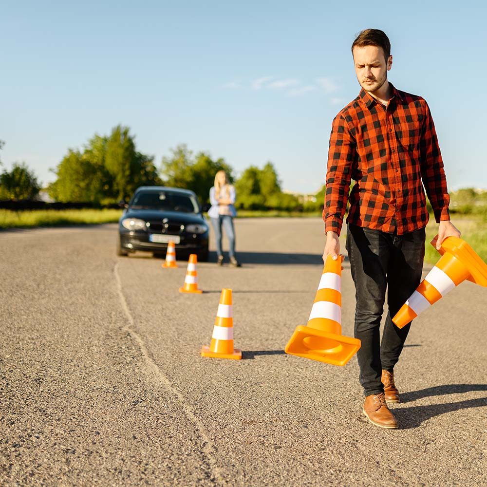 male-instructor-puts-cones-on-road-driving-school-8SHLHPT.jpg